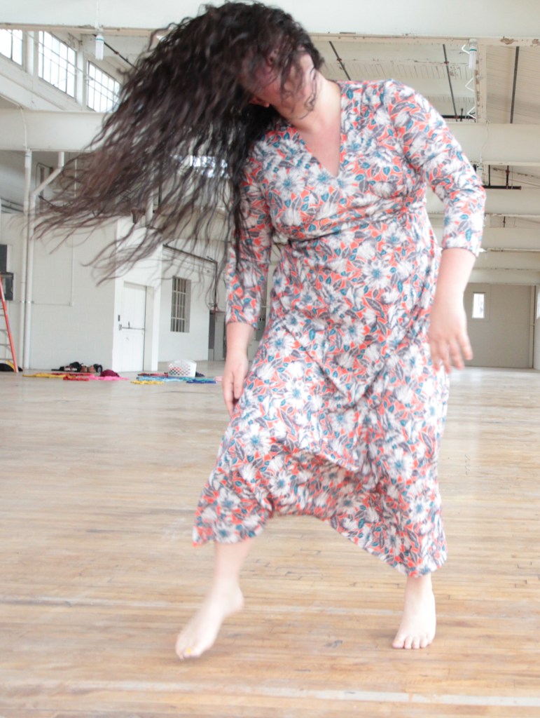 Dancer in a longish patterned dress, fling head and long brown hair flying.