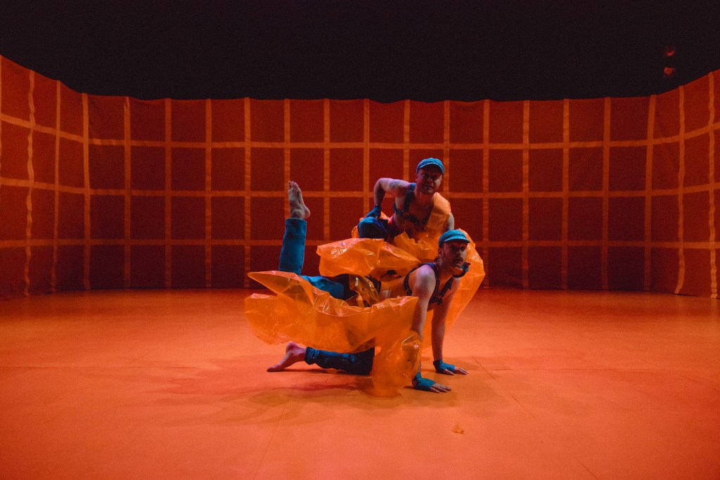 two dancers in a formation in orange light and a grid in the background